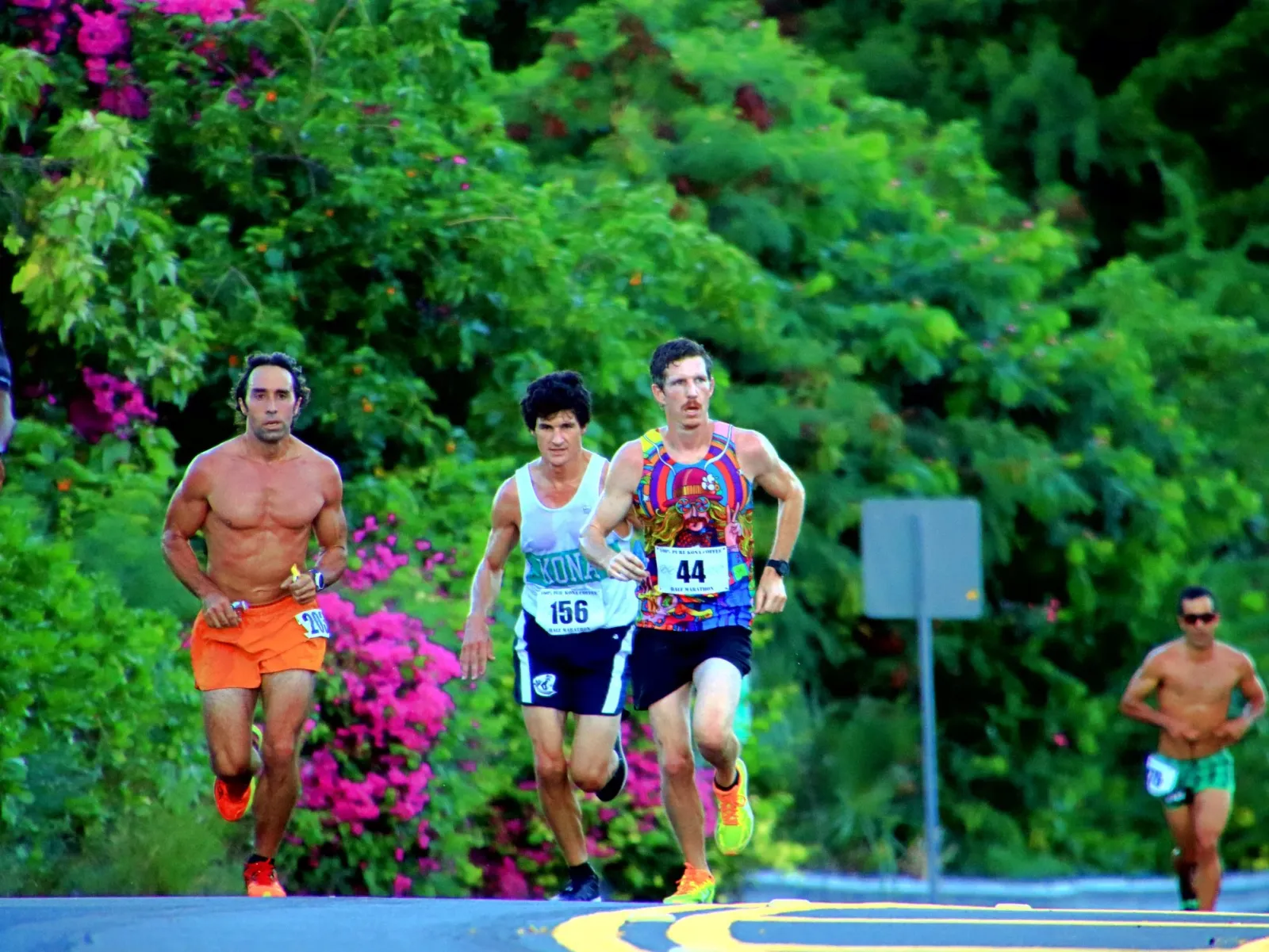 Runners competing in the Kona Coffee Half Marathon with lush greenery and flowers lining the course.