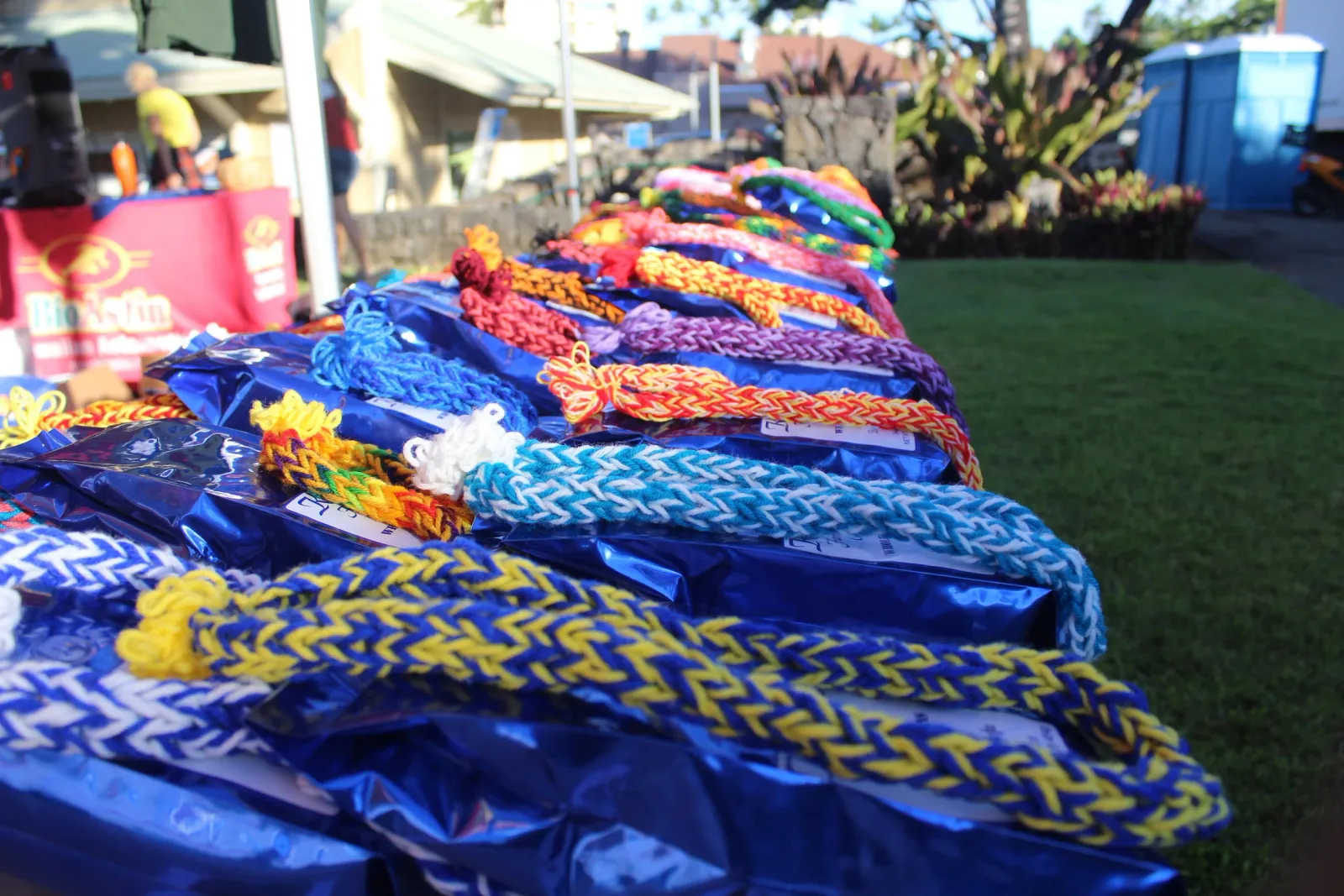 Colorful braided race awards or medals displayed on tables, with people and tents in the background.