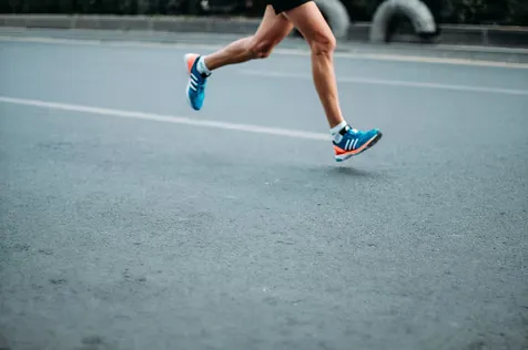 Close-up of a runner's legs and feet as they run on a paved road.