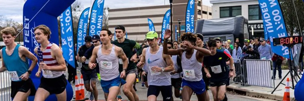 Runners starting a race, with blue inflatable arches and banners in the background.