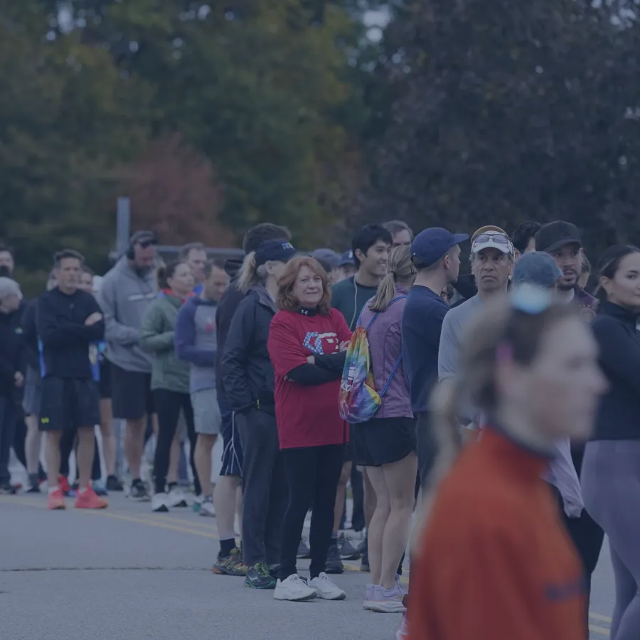 A diverse group of runners stand in a line, some with arms crossed, waiting for a race to begin.