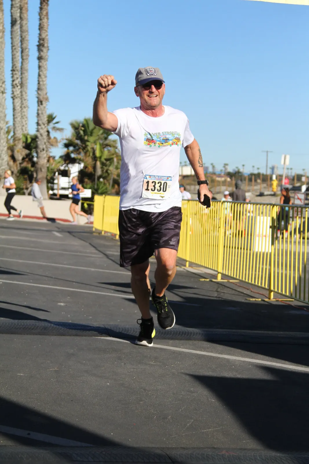 A male runner with bib number 1330 smiles and raises his fist in celebration as he crosses the finish line of the Silver Strand race.