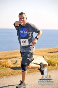 Runner number 66 points at the camera with a determined expression, with the ocean in the background.