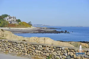 Scenic coastal view with a stone wall in the foreground and a house overlooking the ocean.
