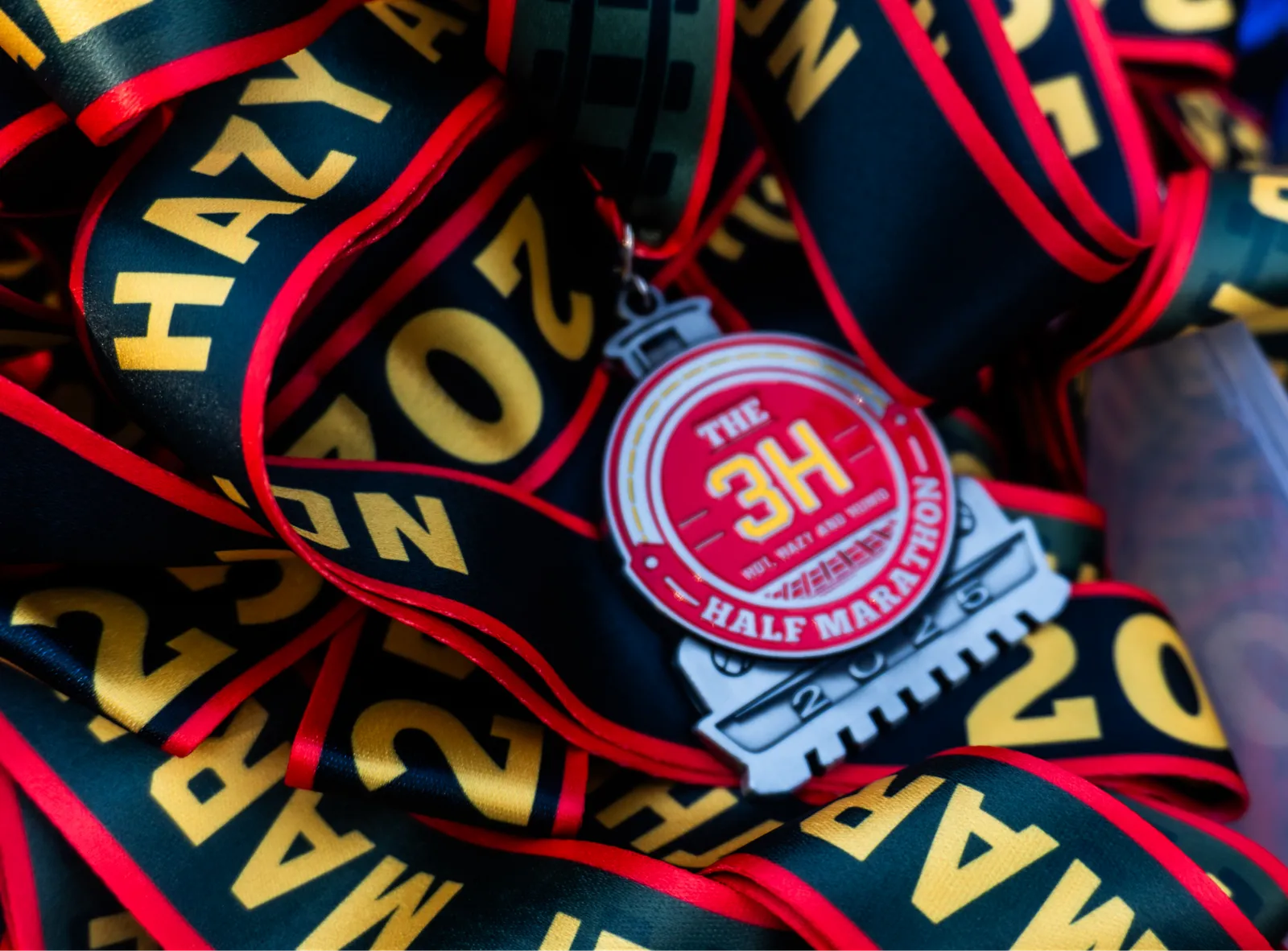 A pile of race medals and ribbons for the 3H Half Marathon, with the year 2025 visible on some ribbons.