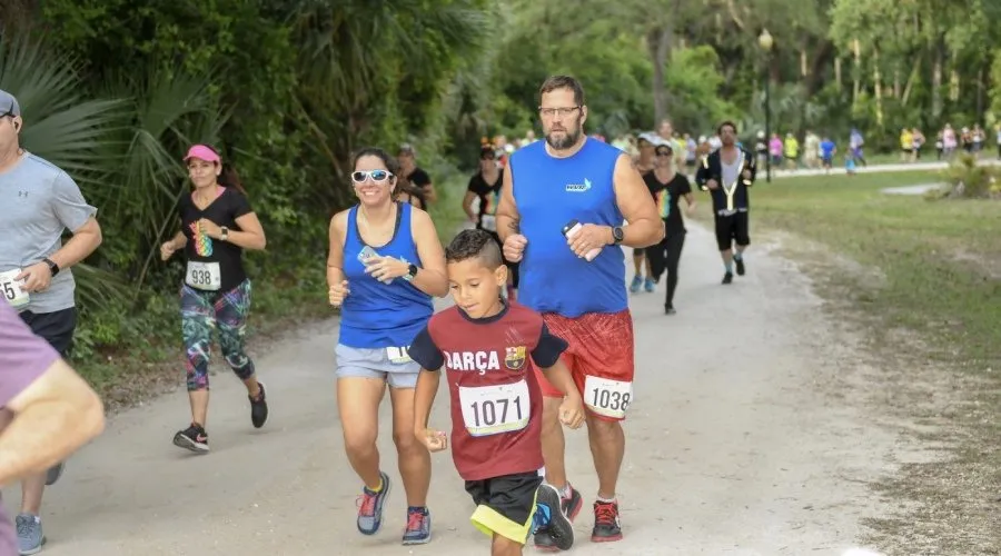 A family, including a young boy, runs on a dirt path during a race, with other runners in the background.
