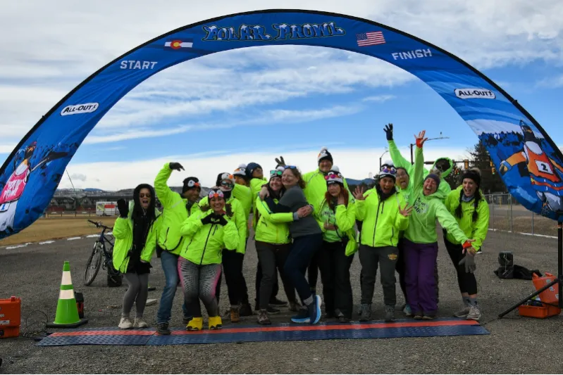 A group of people in bright yellow-green jackets and hats are celebrating under a blue race archway that says 'START' and 'FINISH'.