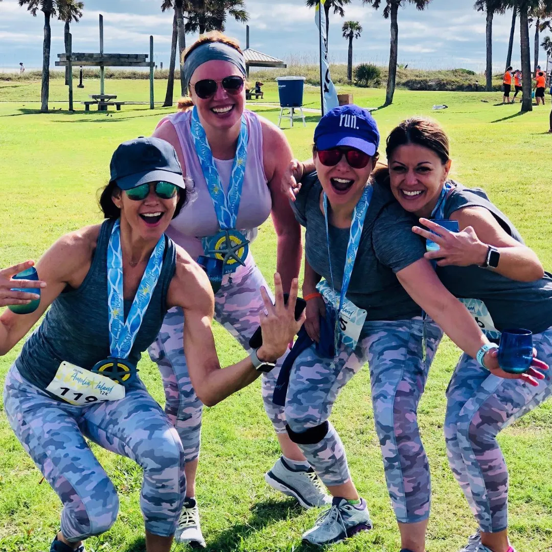 Four women smiling and posing with medals after a race, wearing camouflage running pants and athletic tops.