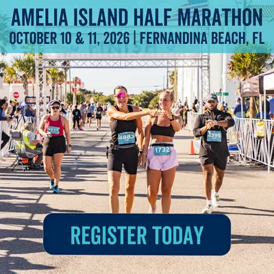 Two women smiling and crossing the finish line at the Amelia Island Half Marathon, with other runners and spectators in the background.