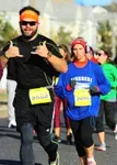 Two runners, one giving a shaka sign, participating in a road race.