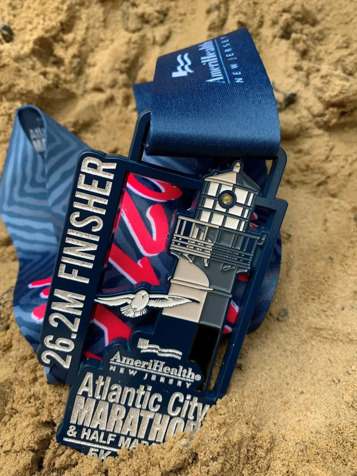 Atlantic City Marathon & Half Marathon medal with a lighthouse design, resting on sand.