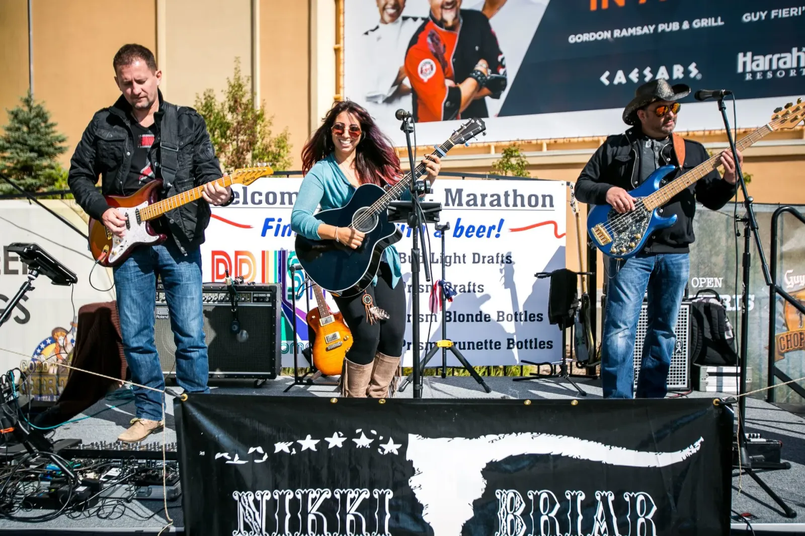 A band performing on a stage with guitars and microphones, with a banner in the background that says 'Marathon' and 'beer!'
