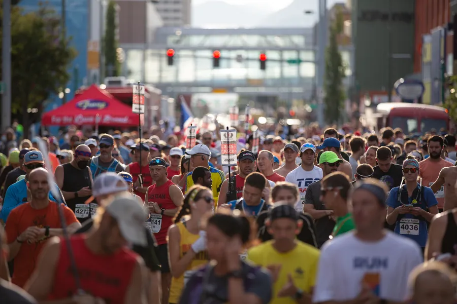 A large group of runners are walking forward on a city street during a race, with buildings and traffic lights in the background.