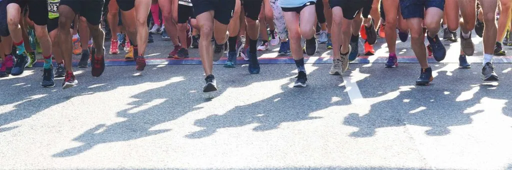 Runners' legs and feet crossing the start line with long shadows cast on the road.