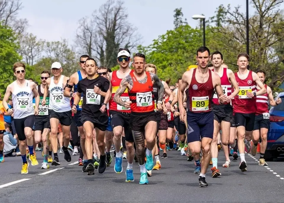 A group of male runners in a race, focused and determined, with bib numbers visible.