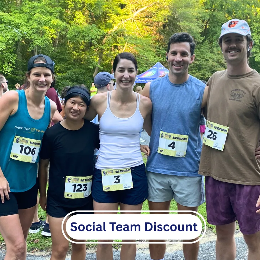 A group of five runners, four women and one man, pose for a photo at a race. They are all smiling and wearing race bibs. The background shows trees and a tent.