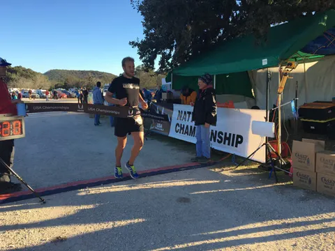 A male runner crosses the finish line at a race, with a banner that reads 'USA Championships' in the background.