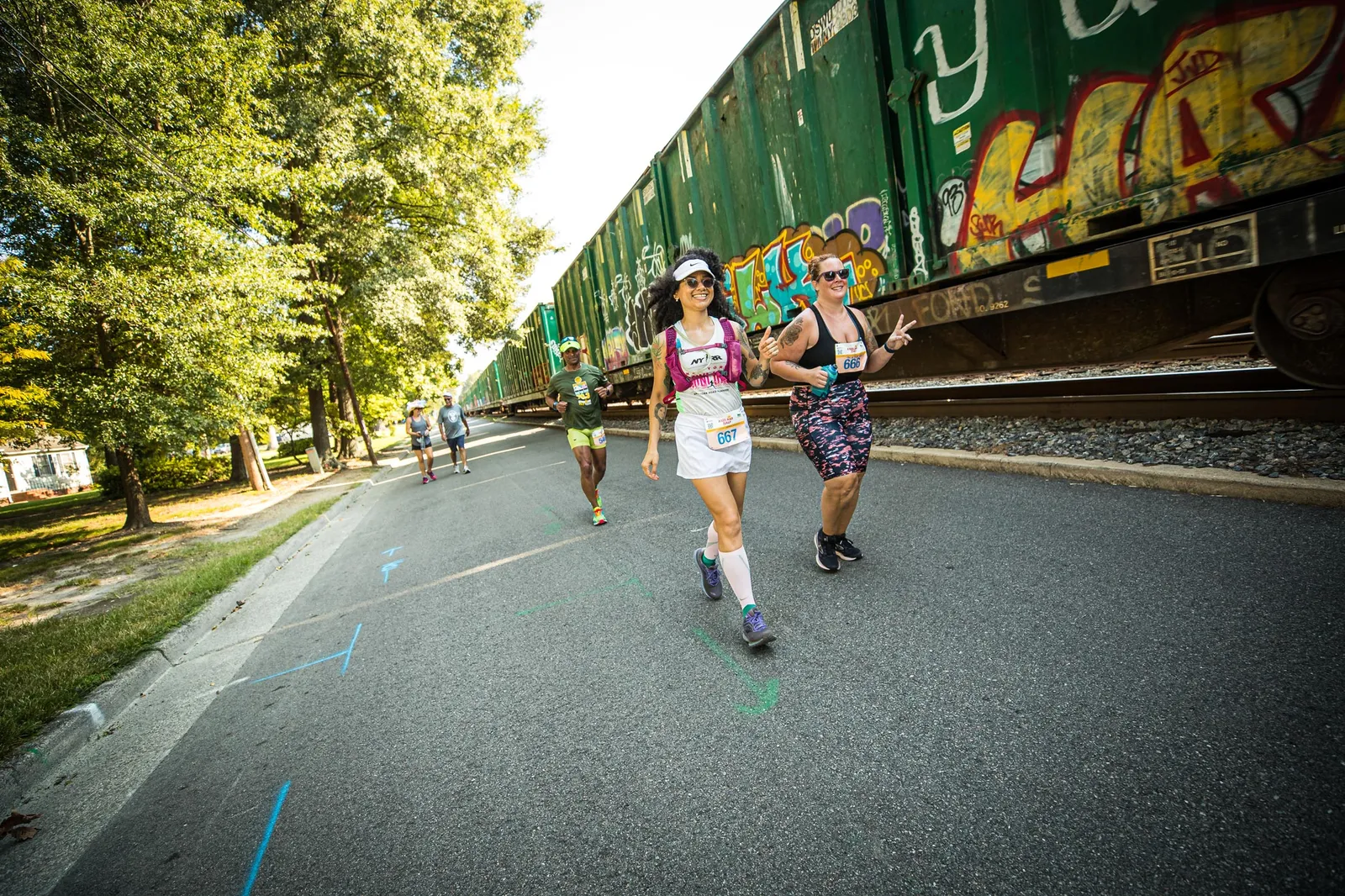 Runners on a road next to a graffiti-covered train.