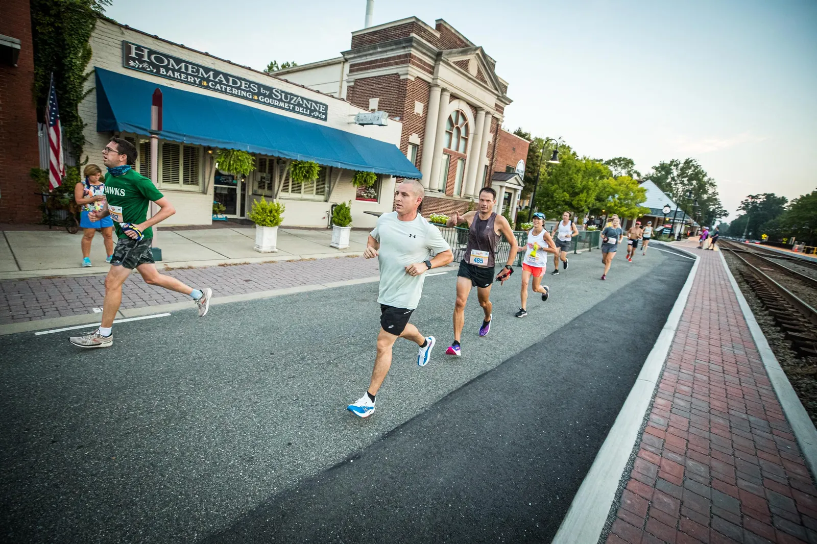 Runners on a road during a race, with buildings and a train track in the background.