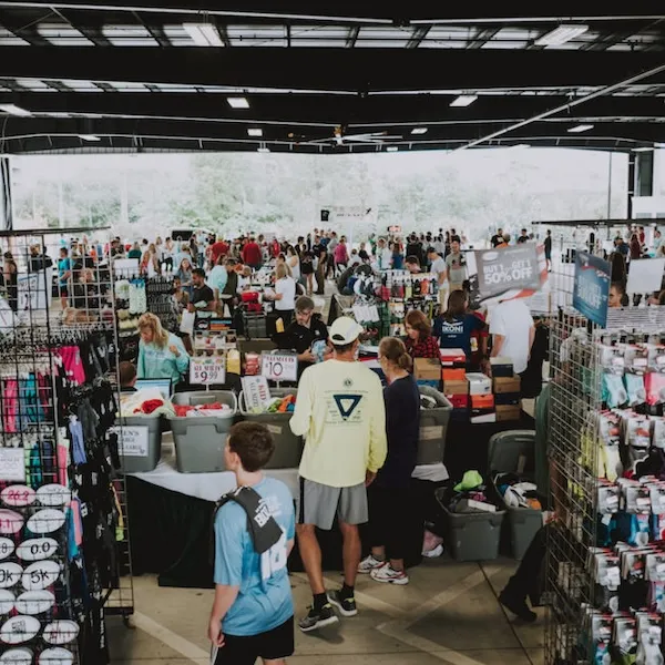 A busy indoor expo with many people browsing stalls selling running gear and apparel.