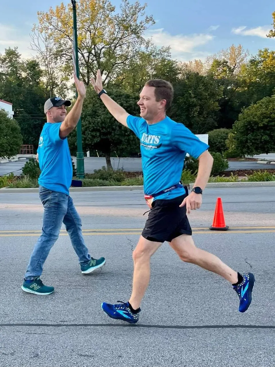 Two male runners in blue shirts high-fiving during a road race.