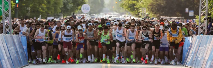 A large group of runners are starting a race, with many focused on the path ahead.