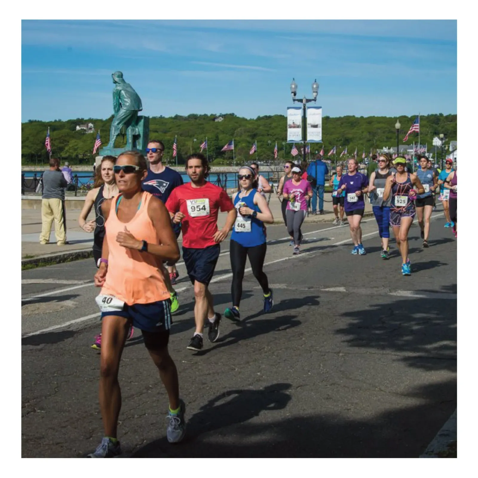 Runners participating in the Barns & Blooms Half Marathon on a sunny day, with a statue and flags in the background.