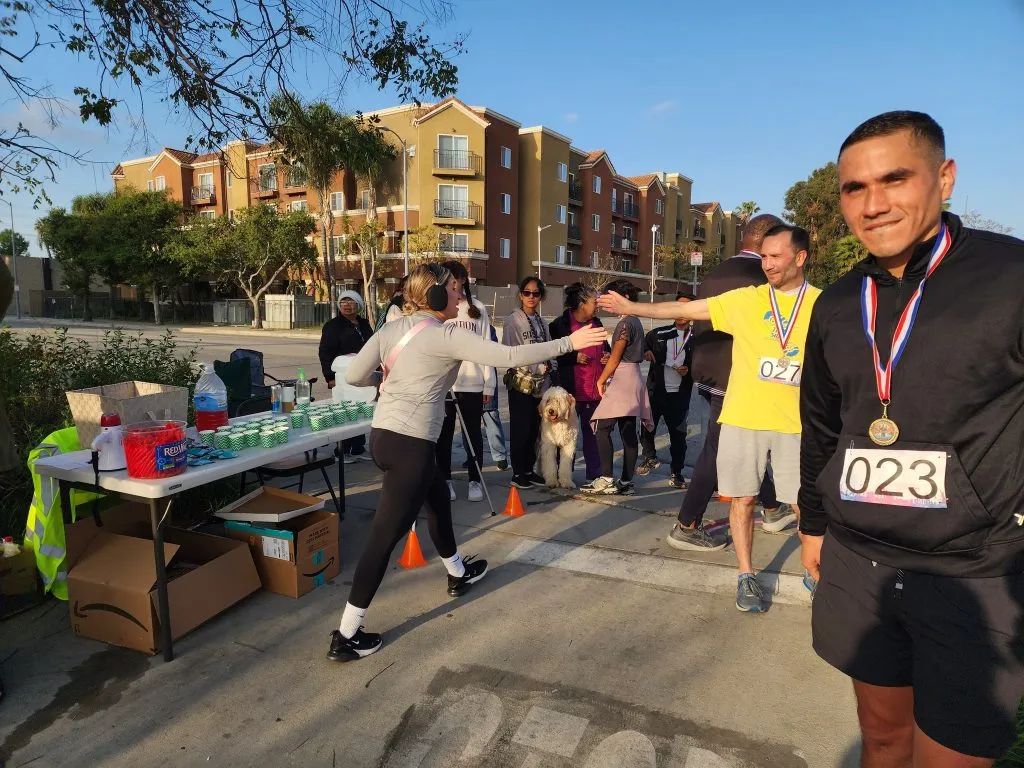 Runners and volunteers at a race aid station, with some runners wearing medals and bib numbers.
