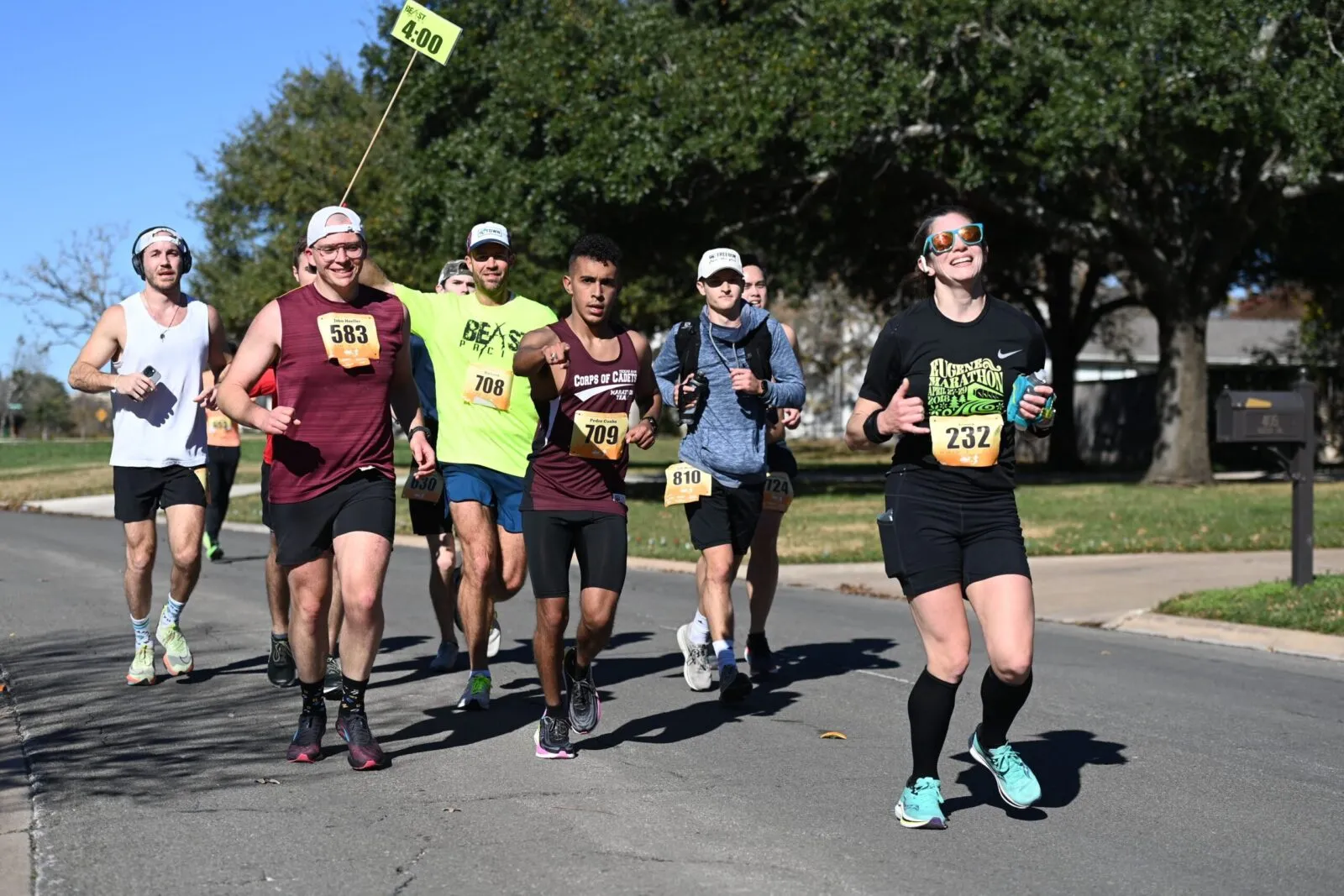 Runners participating in a race on a sunny day, with some runners in the foreground and others in the background.
