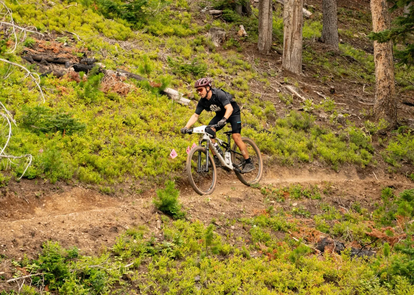 A male runner on a mountain bike navigates a dirt trail through a forest with green foliage.