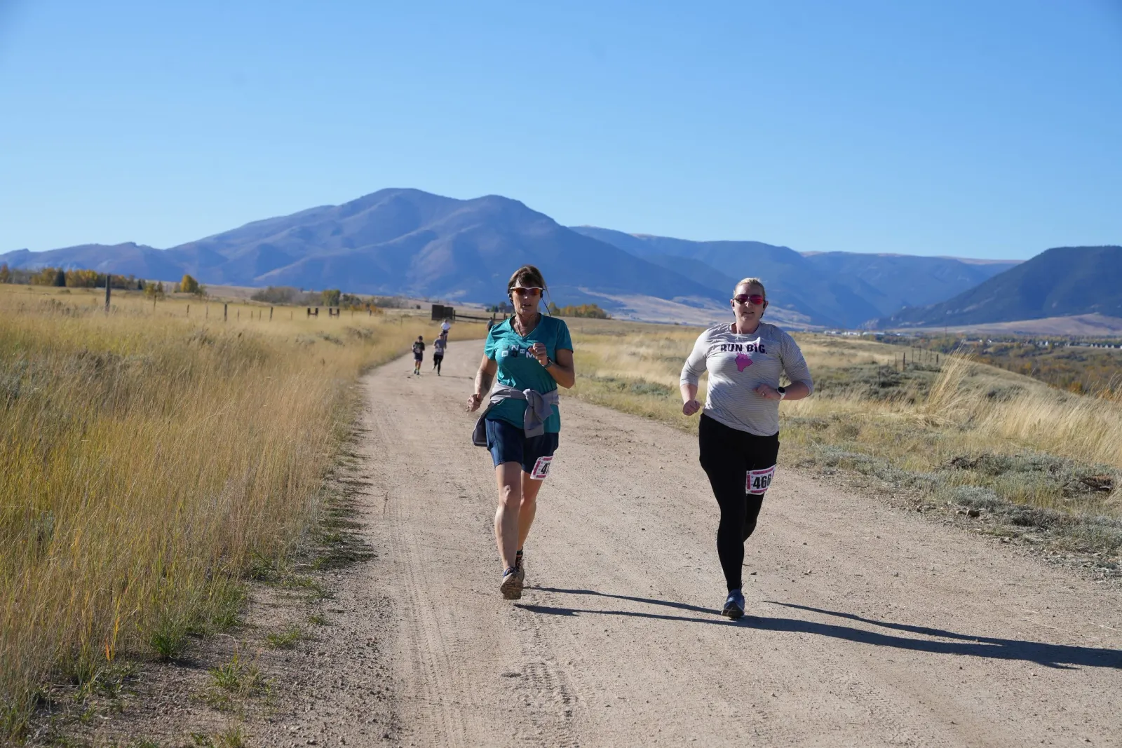 Two female runners on a dirt road with mountains in the background.