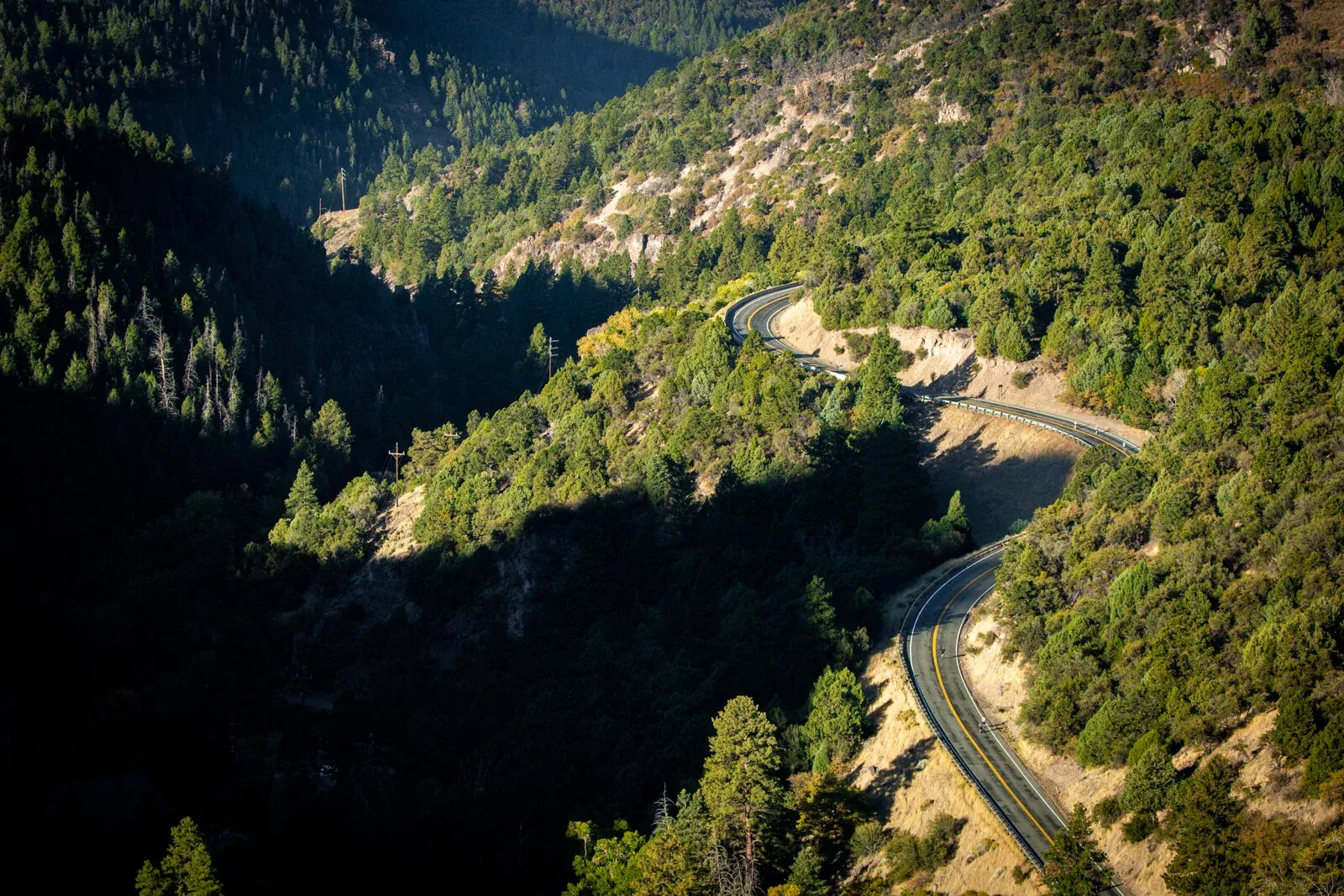 A winding road through a forested canyon, with sunlight and shadows creating a dramatic landscape.