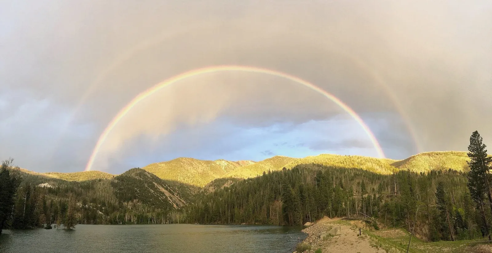 A scenic view of mountains, a lake, and a double rainbow over the landscape.