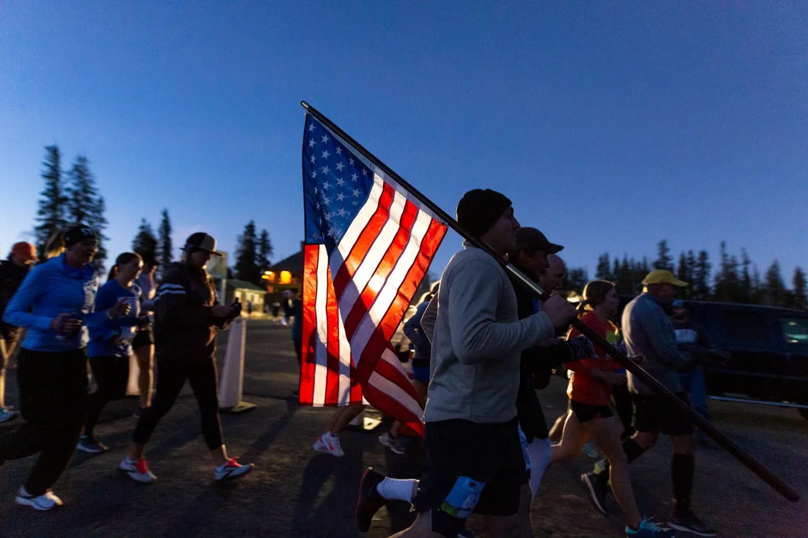 Runners at the start line of a race, with one person carrying an American flag.