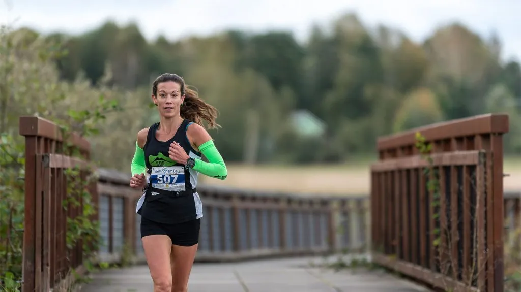A female runner with bib number 507 runs on a wooden boardwalk with trees in the background.