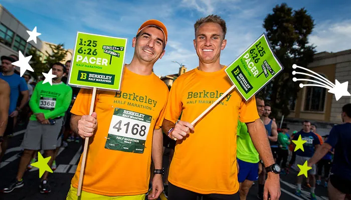 Two smiling men in orange shirts holding 'Pacer' signs at the start of the Berkeley Half Marathon.