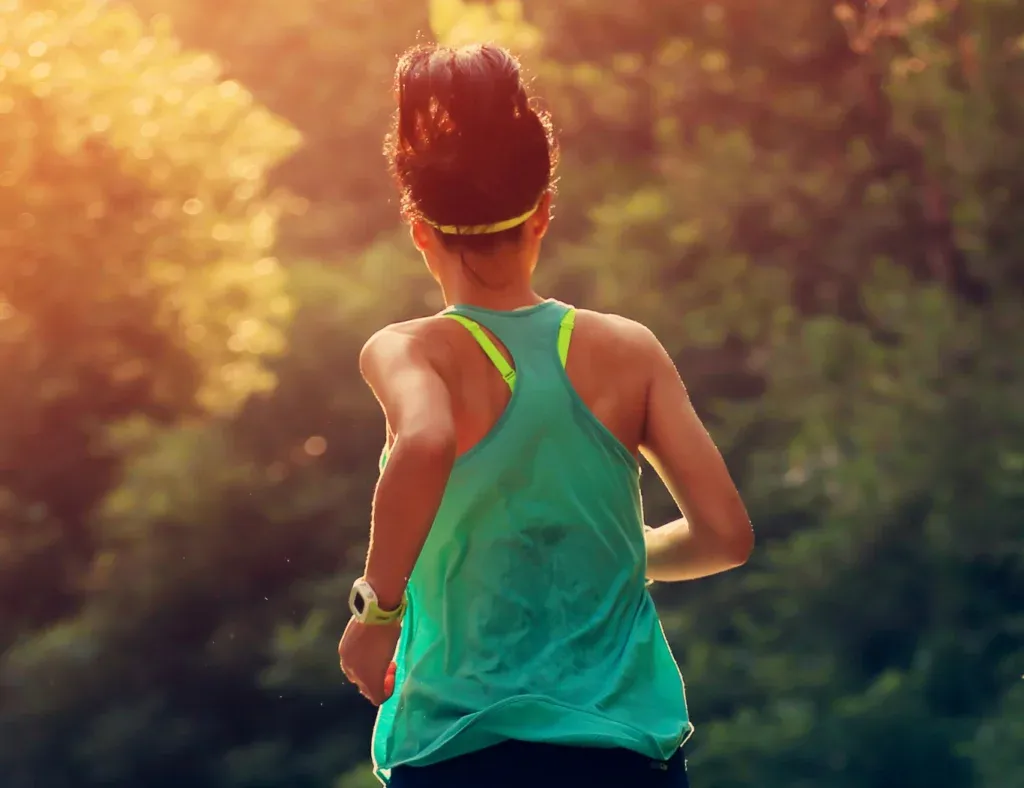 Runner from behind on a trail with sun flare.