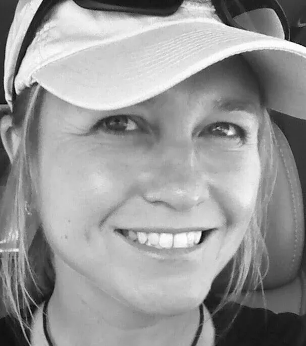 Close-up of a smiling woman wearing a white visor and sunglasses.