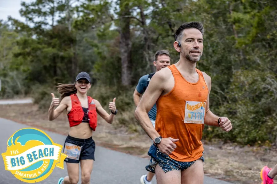 A male runner in an orange tank top and a female runner giving a thumbs-up, both participating in the Big Beach Marathon & Half.