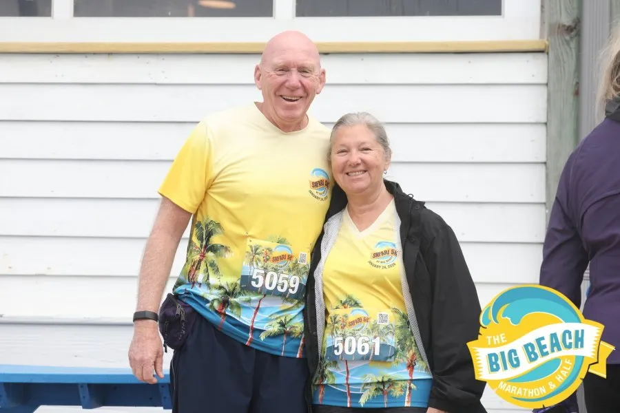 A smiling couple wearing matching yellow race shirts with a tropical design and bib numbers.