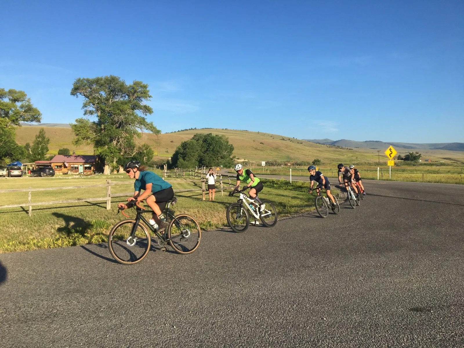 Cyclists riding on a road with scenic hills in the background.