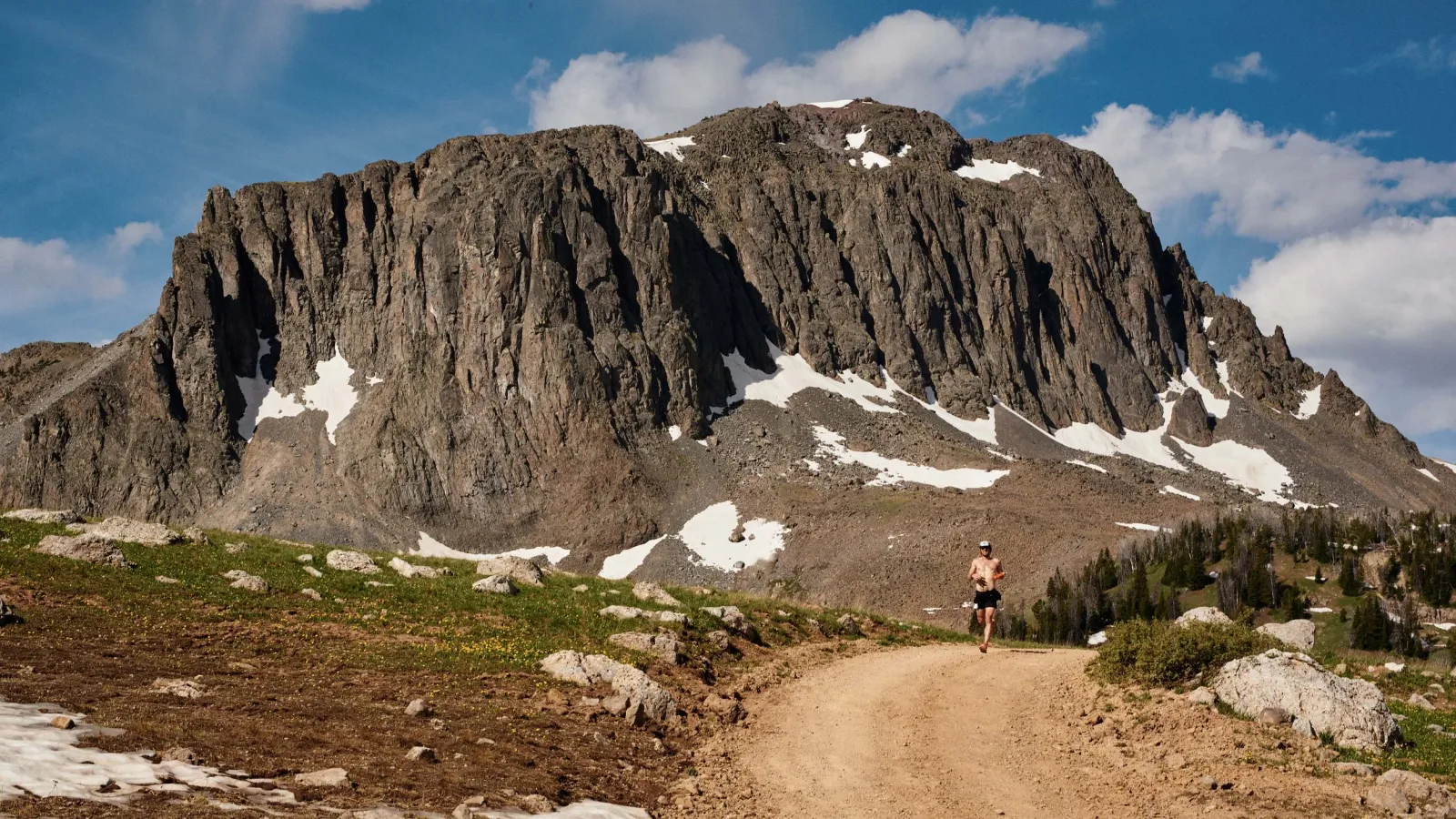 A solo runner on a dirt trail with a large, rugged mountain in the background.