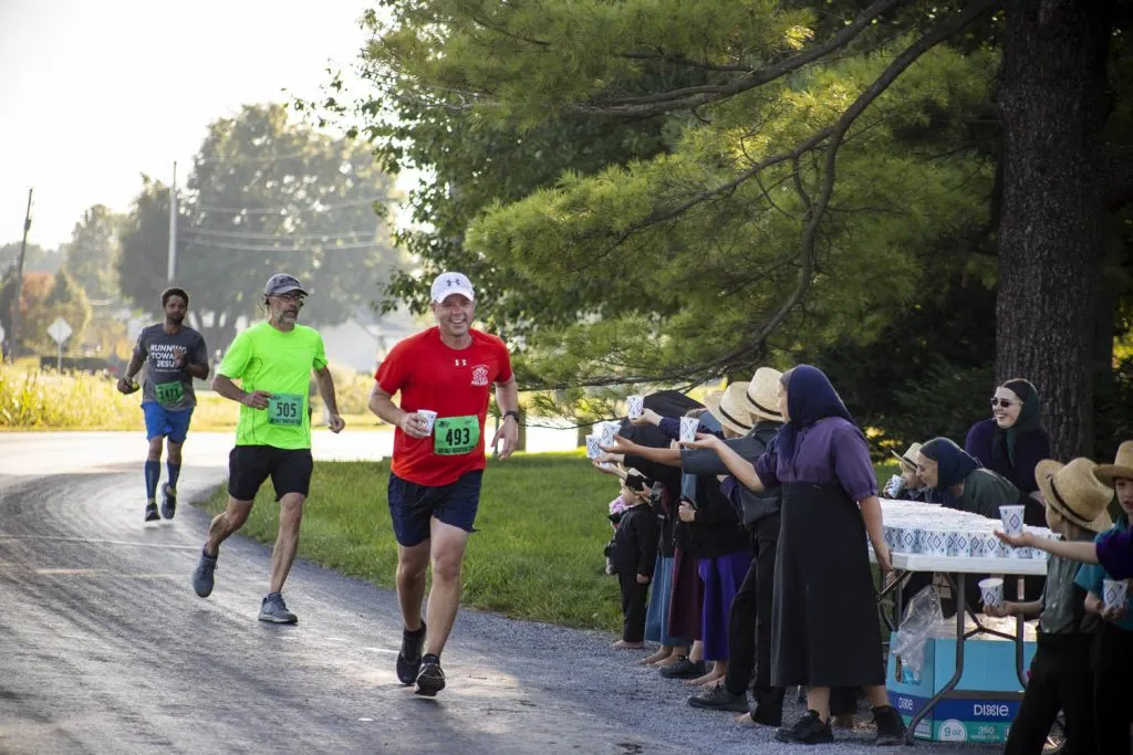 Runners receive cups from spectators along the side of a road during a race.