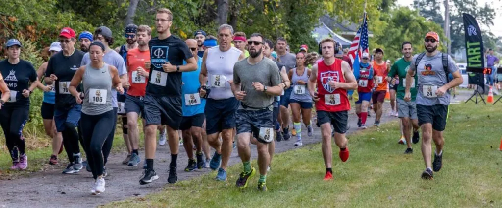 A group of runners starting a race, with some in the foreground and others further back on a path lined with trees.