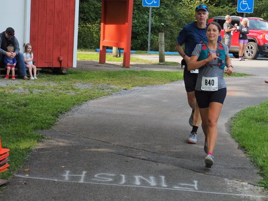 A female runner with bib number 840 and a male runner behind her are running on a paved path with 'FINISH' written on it in white chalk.