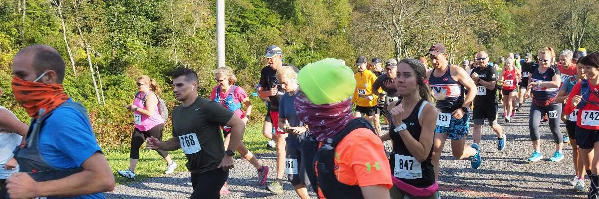 A group of runners in colorful racing attire are starting a race, with trees and foliage in the background.