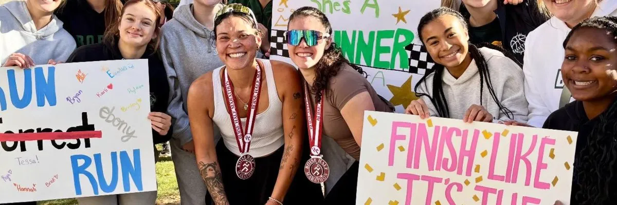 A group of smiling runners, some wearing medals, hold up signs that say 'RUN' and 'FINISH LIKE TT'S THE'.