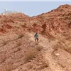 A lone runner navigates a steep, rocky trail on a mountainside under a clear blue sky.
