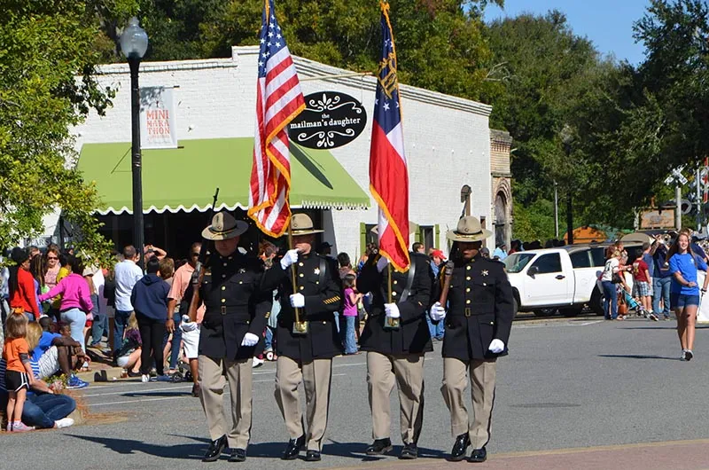 A parade with uniformed individuals carrying flags, and spectators watching from the side of the street.