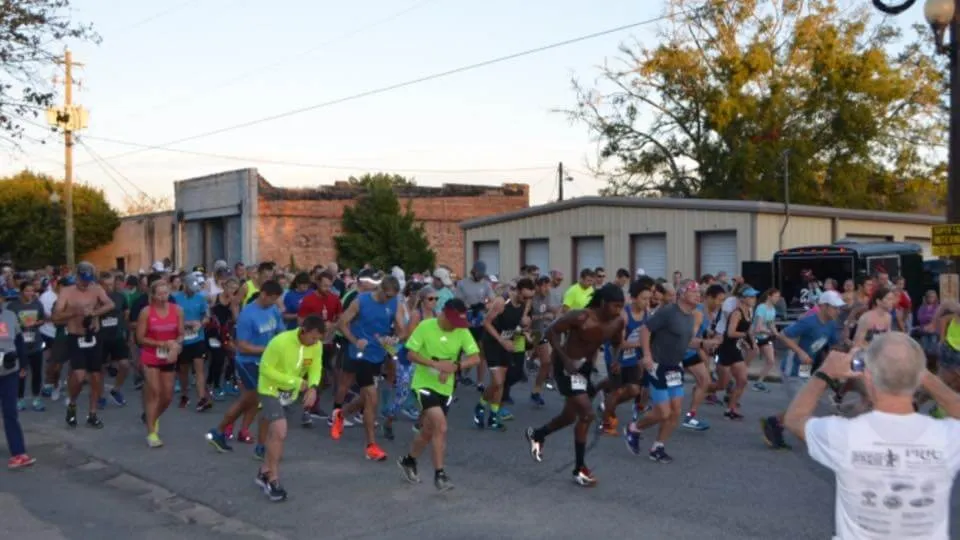 A large group of runners starting a race on a road, with buildings and trees in the background.